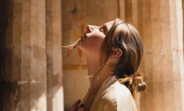 A woman in a beige coat looks up inside ancient Egyptian temple ruins.