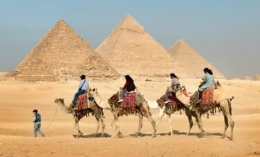Tourists riding camels near the Great Pyramids of Giza, Egypt under clear skies.